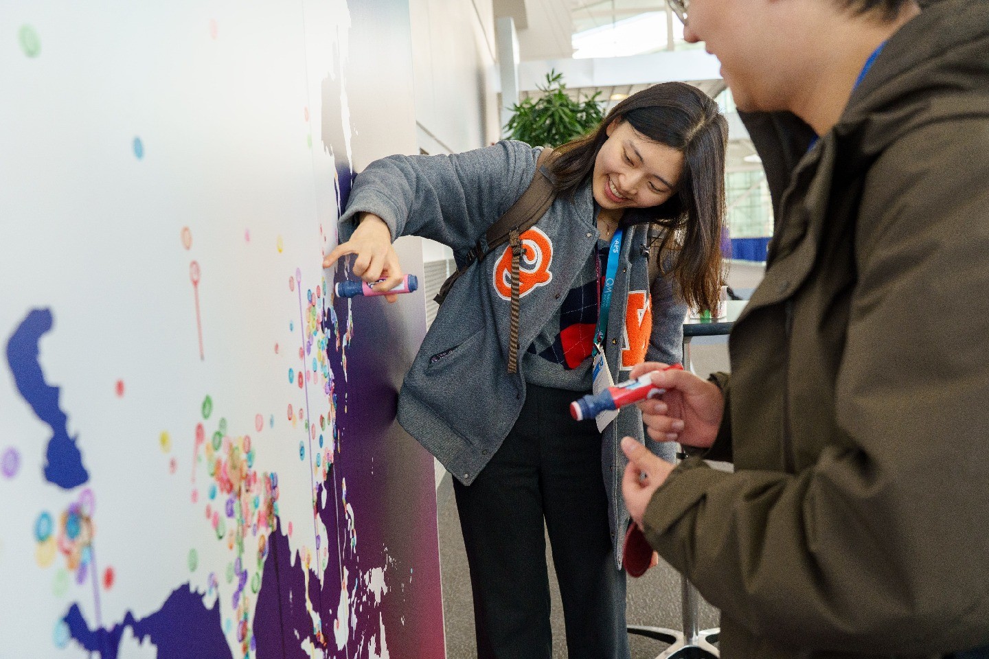 A Global Physics Summit attendee smiles while marking on a large colorful map where she's from.