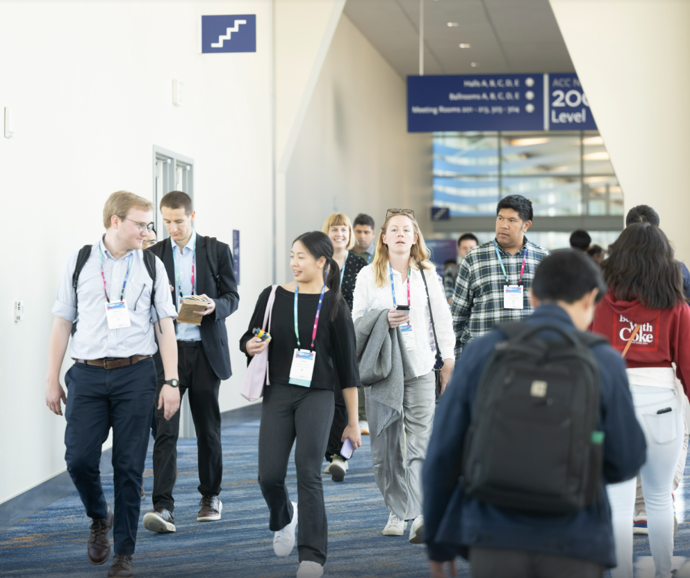 A group of people wearing conference badges and moving the same direction through a hallway