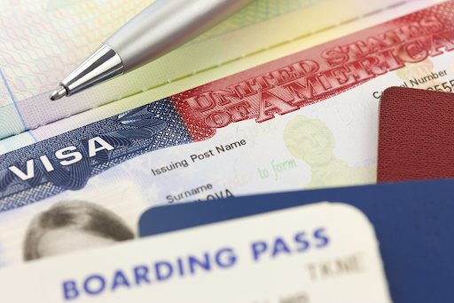A pen and stack of papers including an American Visa and a boarding pass.