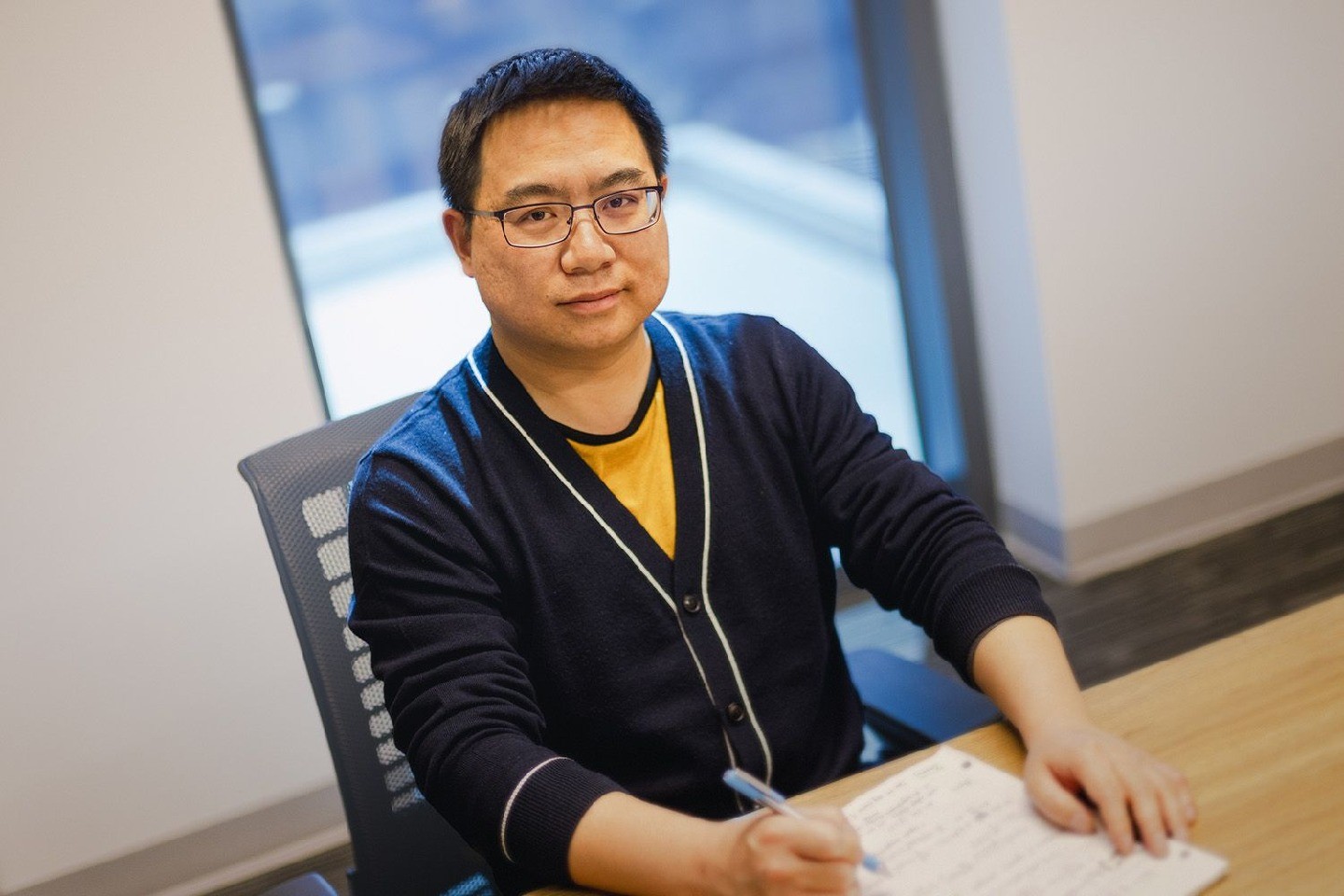 Fan Zhang sits at a desk with a pen and paper in front of him.