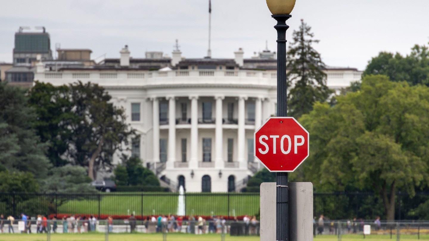 A photo of the US White House that includes a stop sign in the frame
