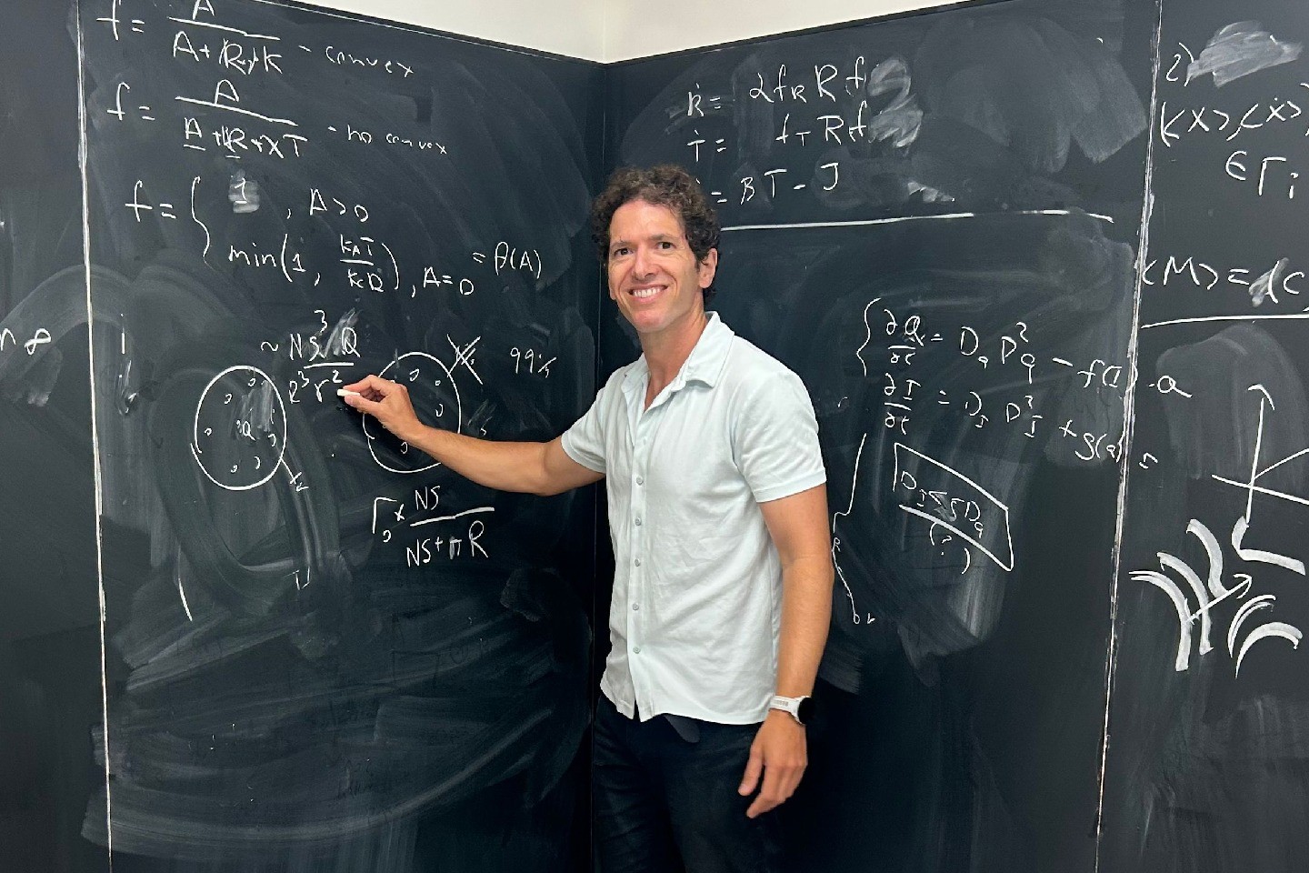 Ariel Amir holds chalk at a chalkboard with equations on it.