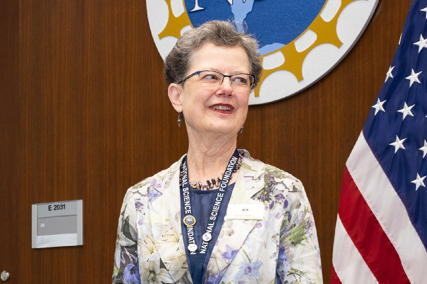 Julia Phillips smiles in front of an American flag and the National Science Foundation logo.