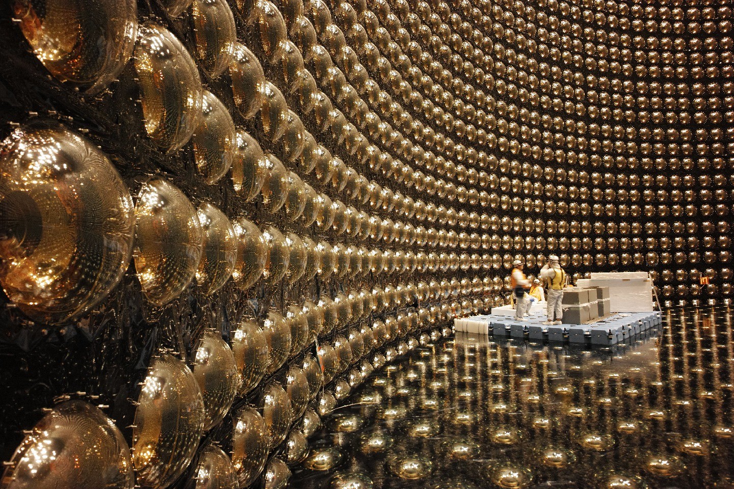Workers on a raised platform inspect thousands of golden photomultiplier tubes lining the curved interior walls of the Super-Kamiokande detector tank.
