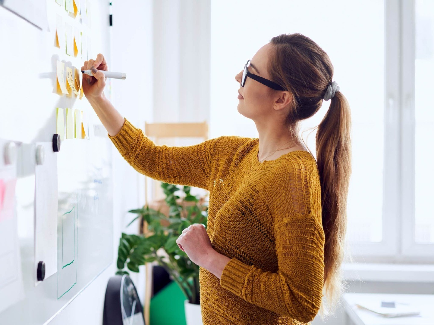 A woman participating in a meeting by writing on a Post-It note on a whiteboard