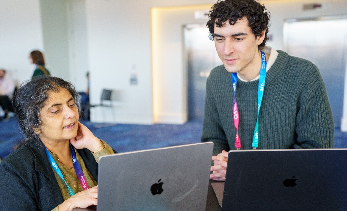 An older woman and a younger man looking at laptops together while attending the APS Global Physics Summit