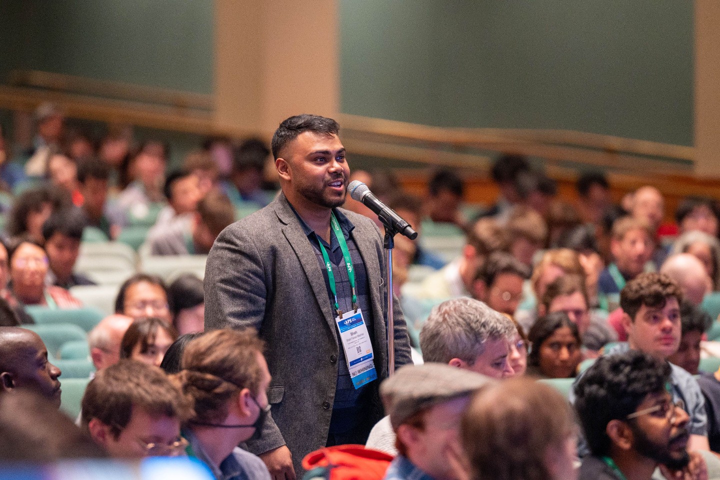 An individual speaking at a microphone during a Q&A session at an APS meeting