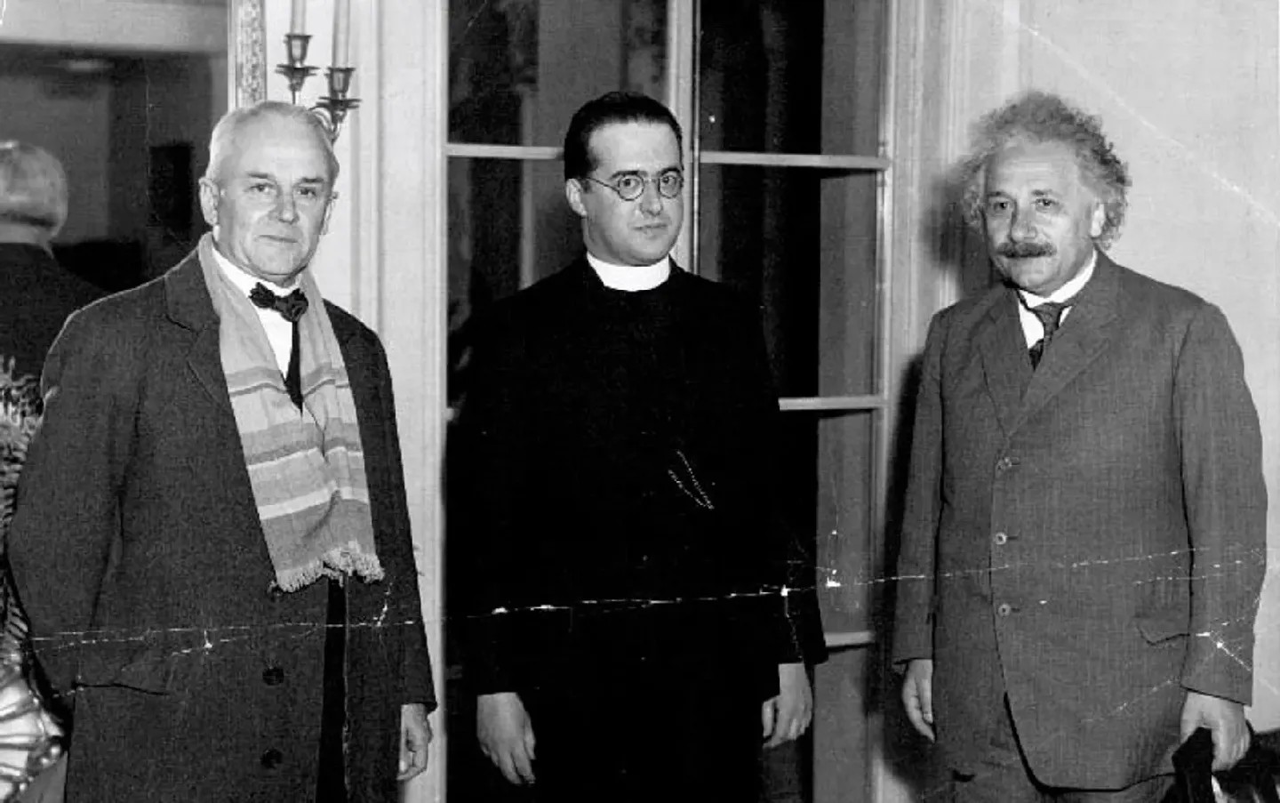 A black-and-white photo of the three men — from left to right, Millikan, Lemaître,  and Einstein — standing in a row, looking at the camera.