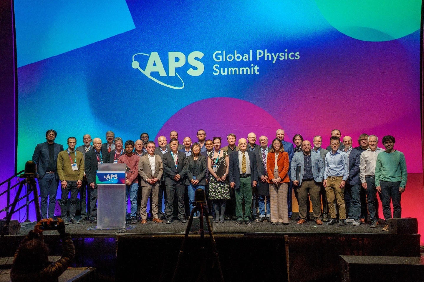 A group standing on a stage and in front of a background that says APS Global Physics Summit