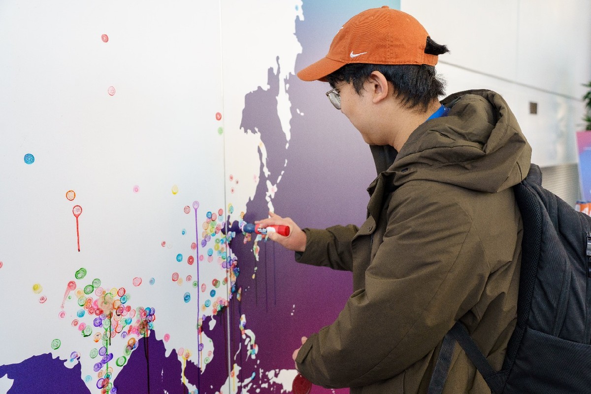 A student in an orange hat marking where he is from on a map of Asia