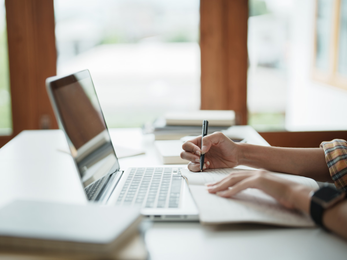 A person looking at a laptop and taking notes