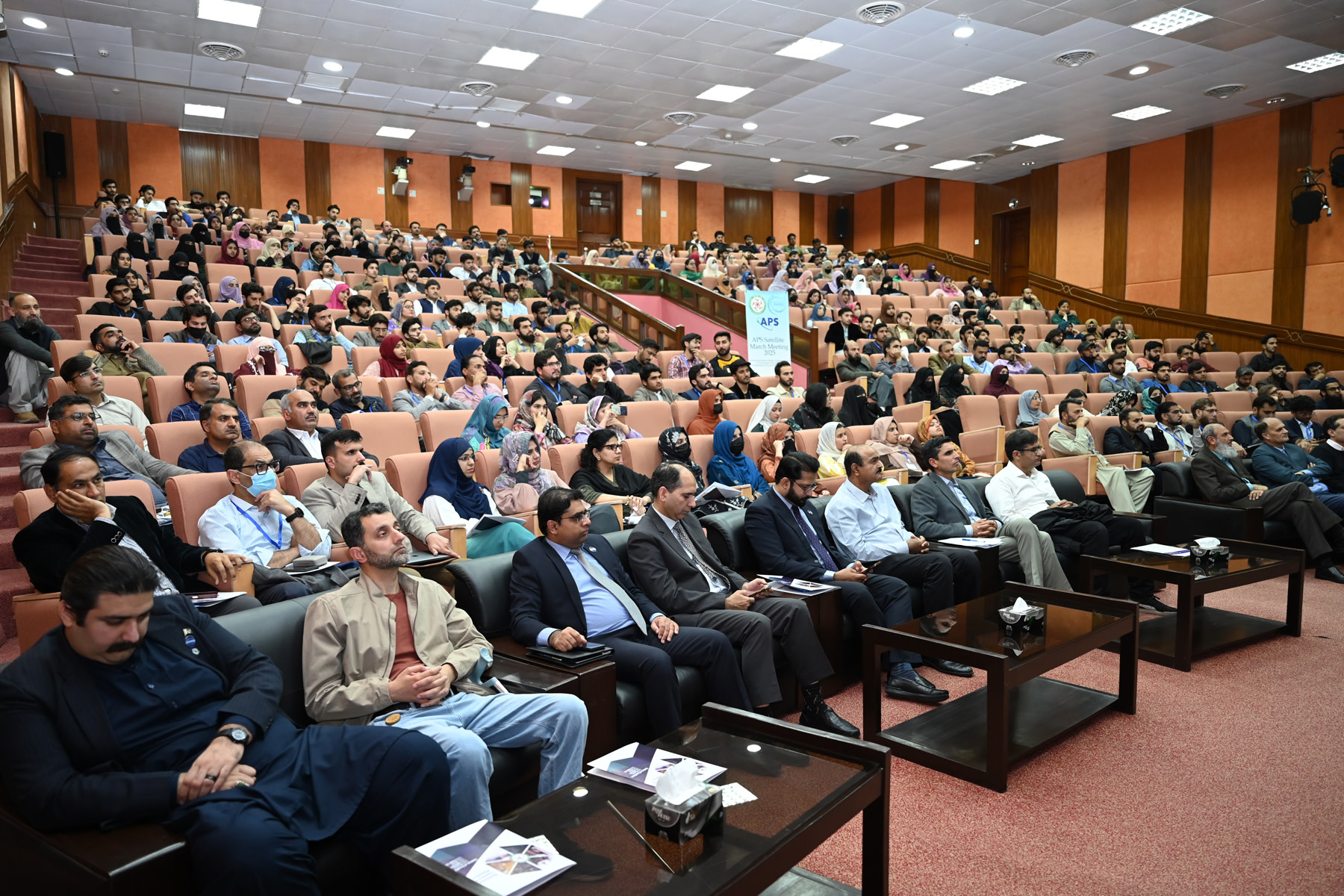 Packed auditorium at a satellite location, with attendees filling theater-style seating.