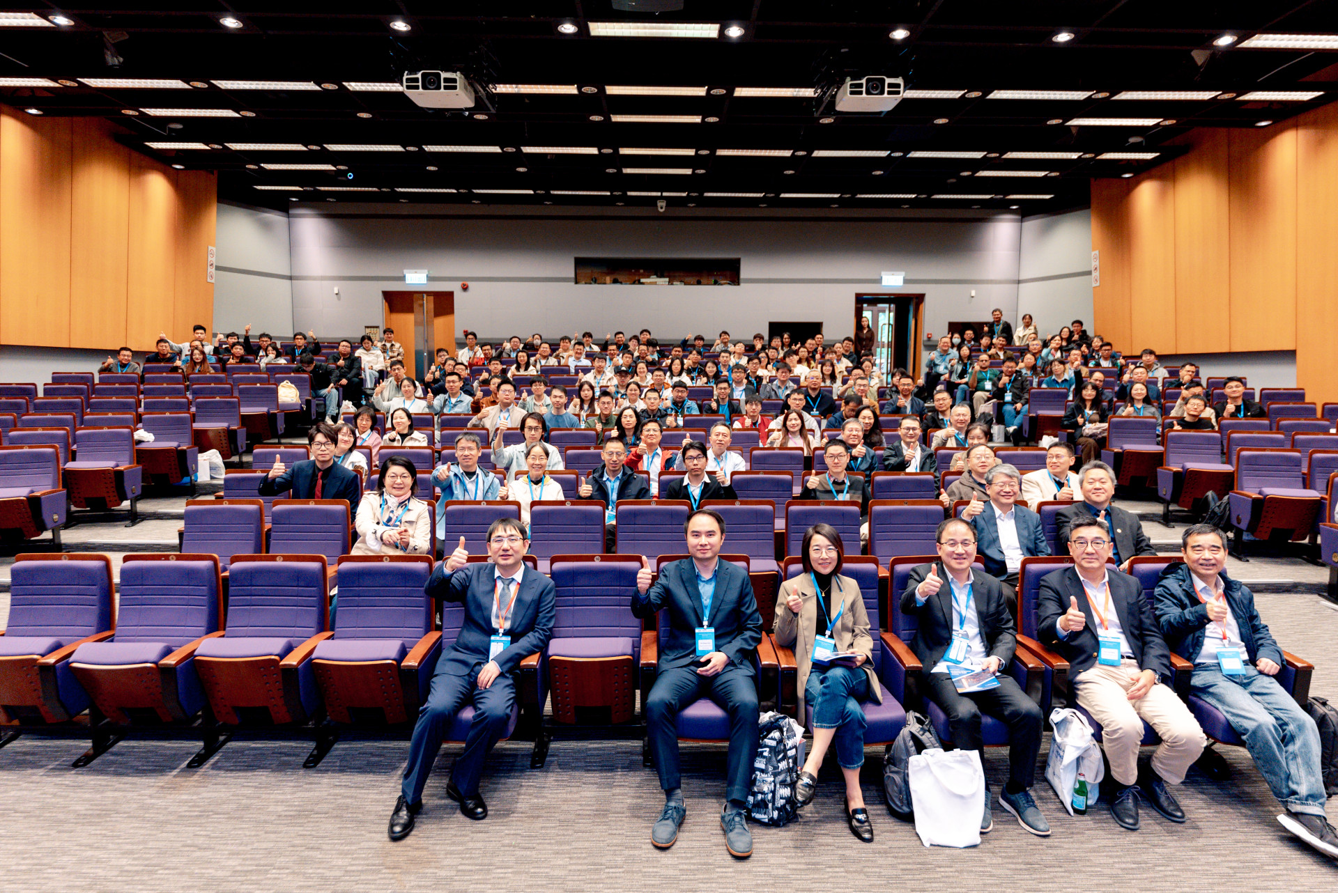Packed auditorium at a satellite location, with attendees filling theater-style seating with thumbs up.