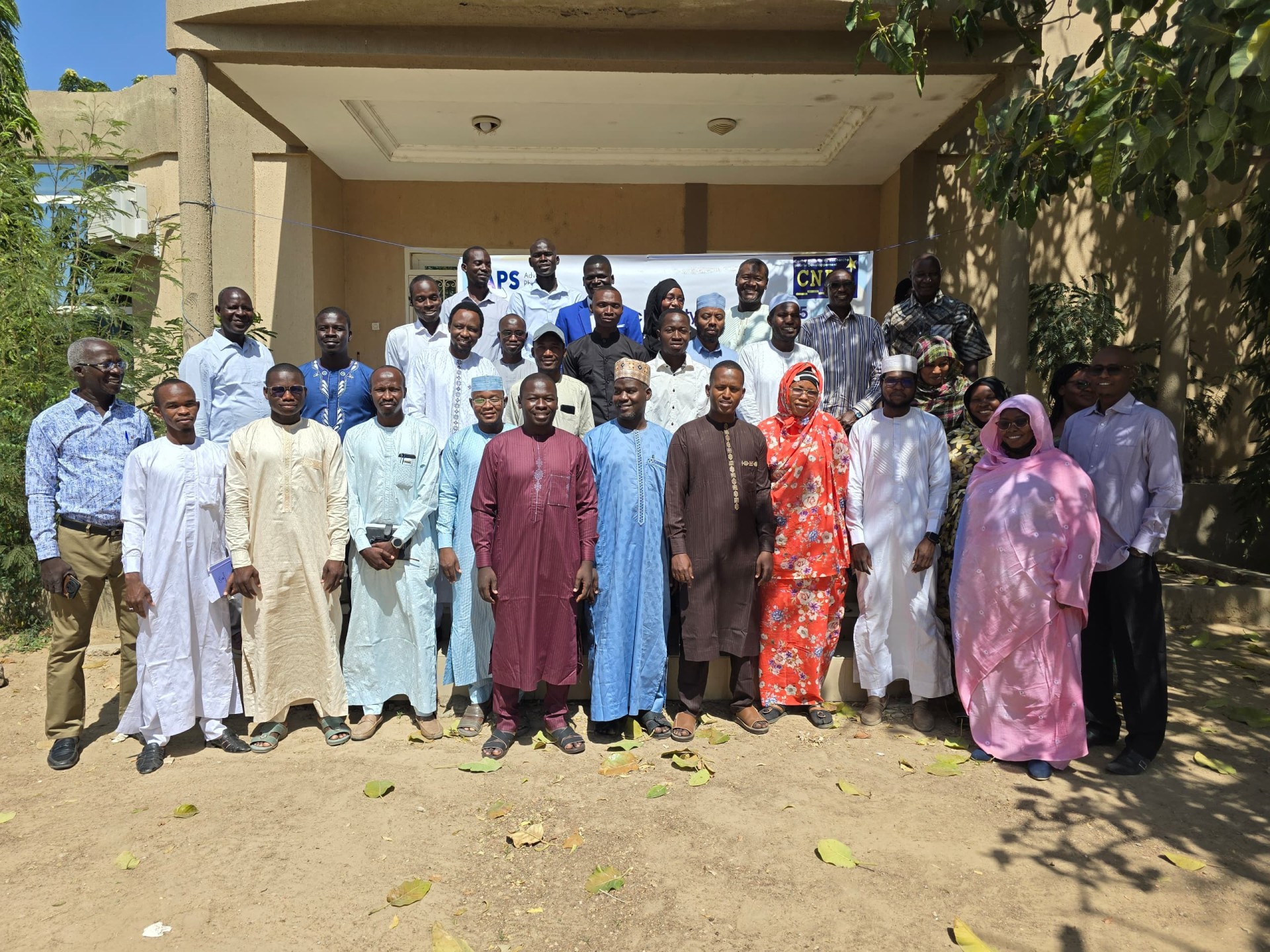 Group photo of satellite site participants, standing outside in front of a building.
