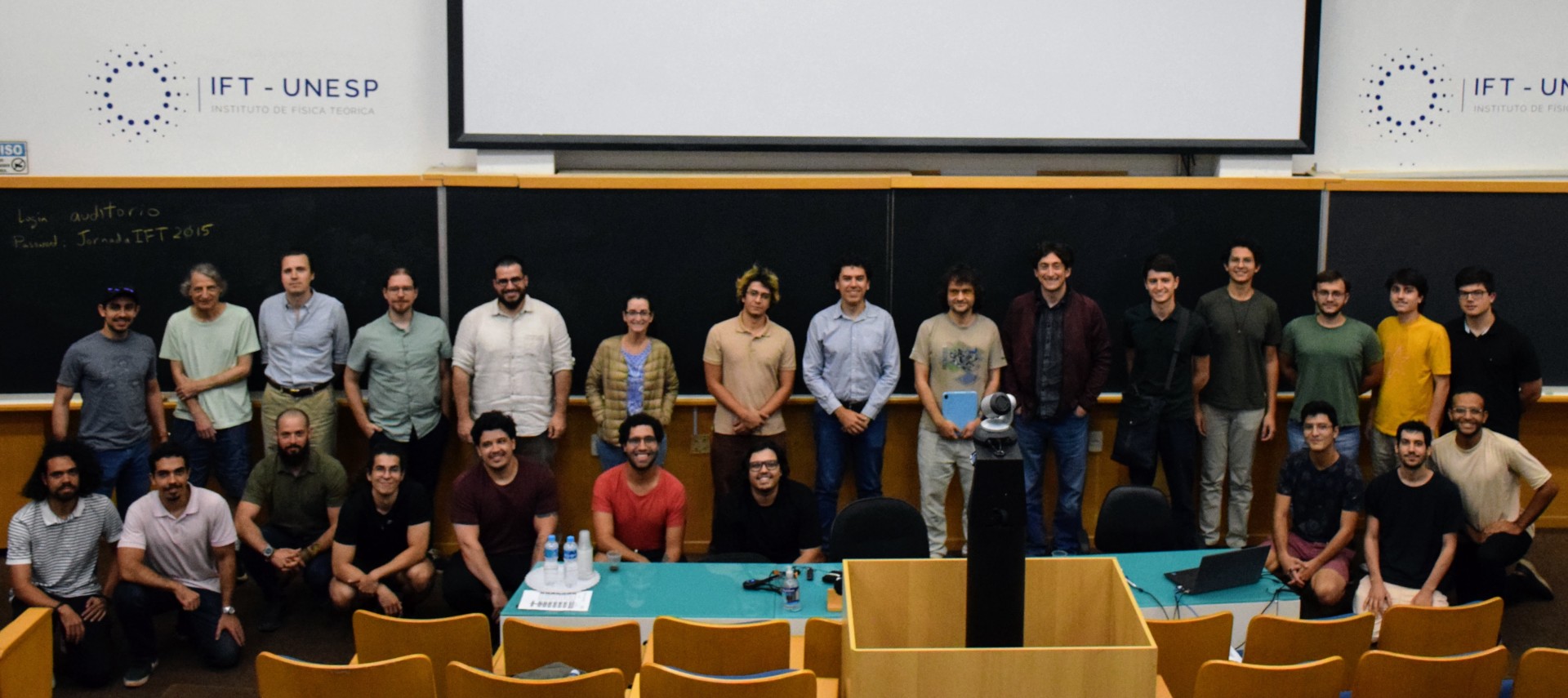 Group photo of physics students and faculty gathered in front of a projection screen.