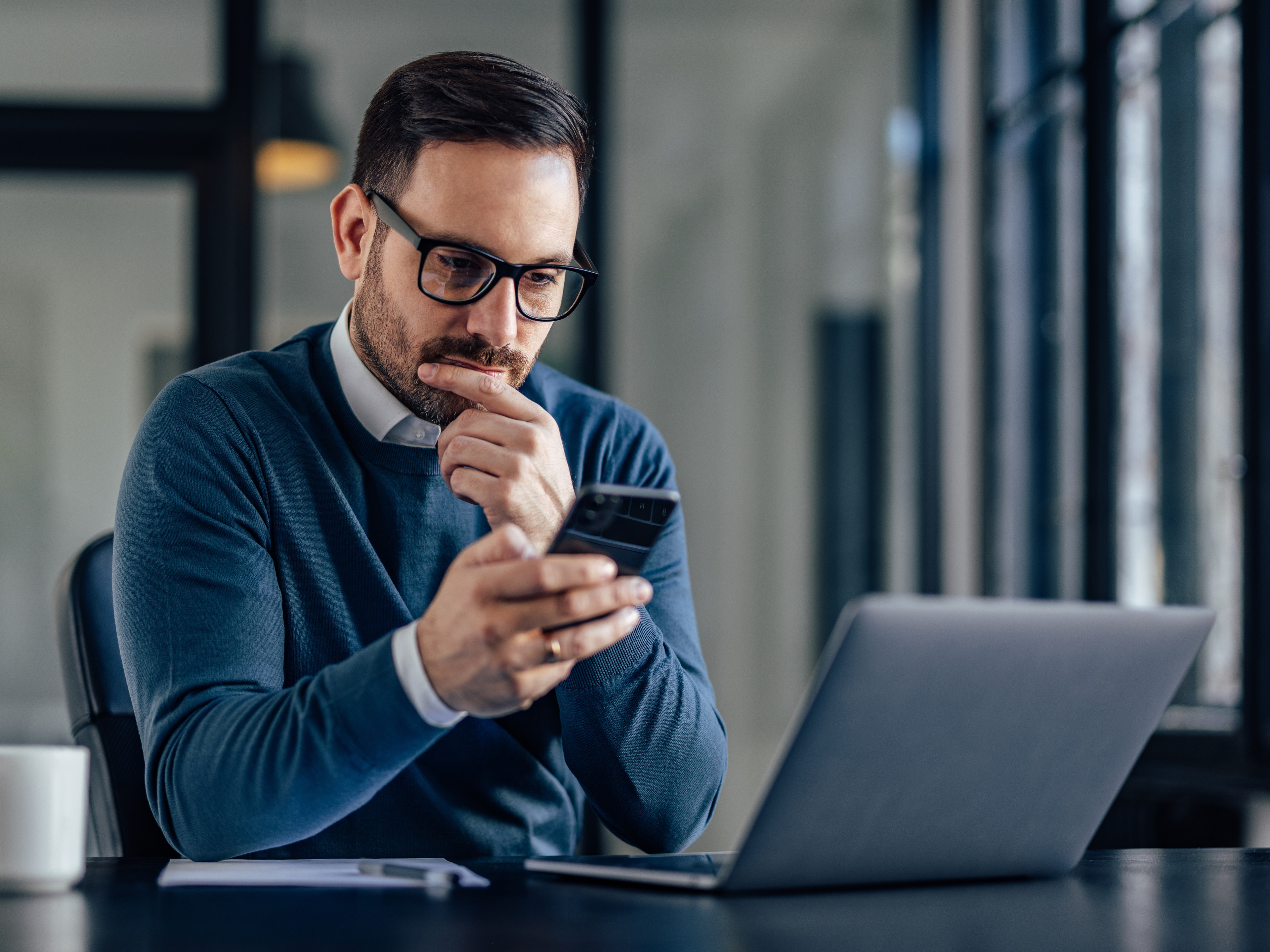 A person sitting at a computer while looking at a smartphone