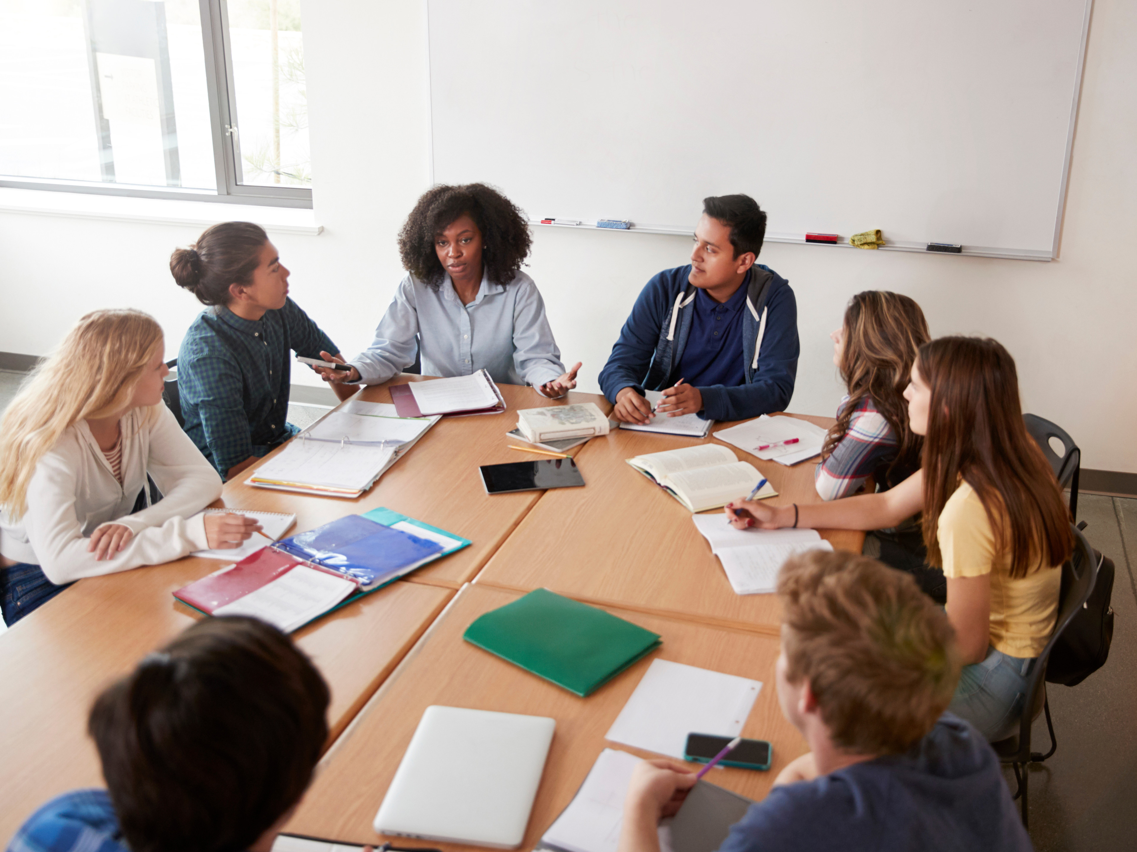 Eight young adults gathered in a group discussion at a table, some taking notes