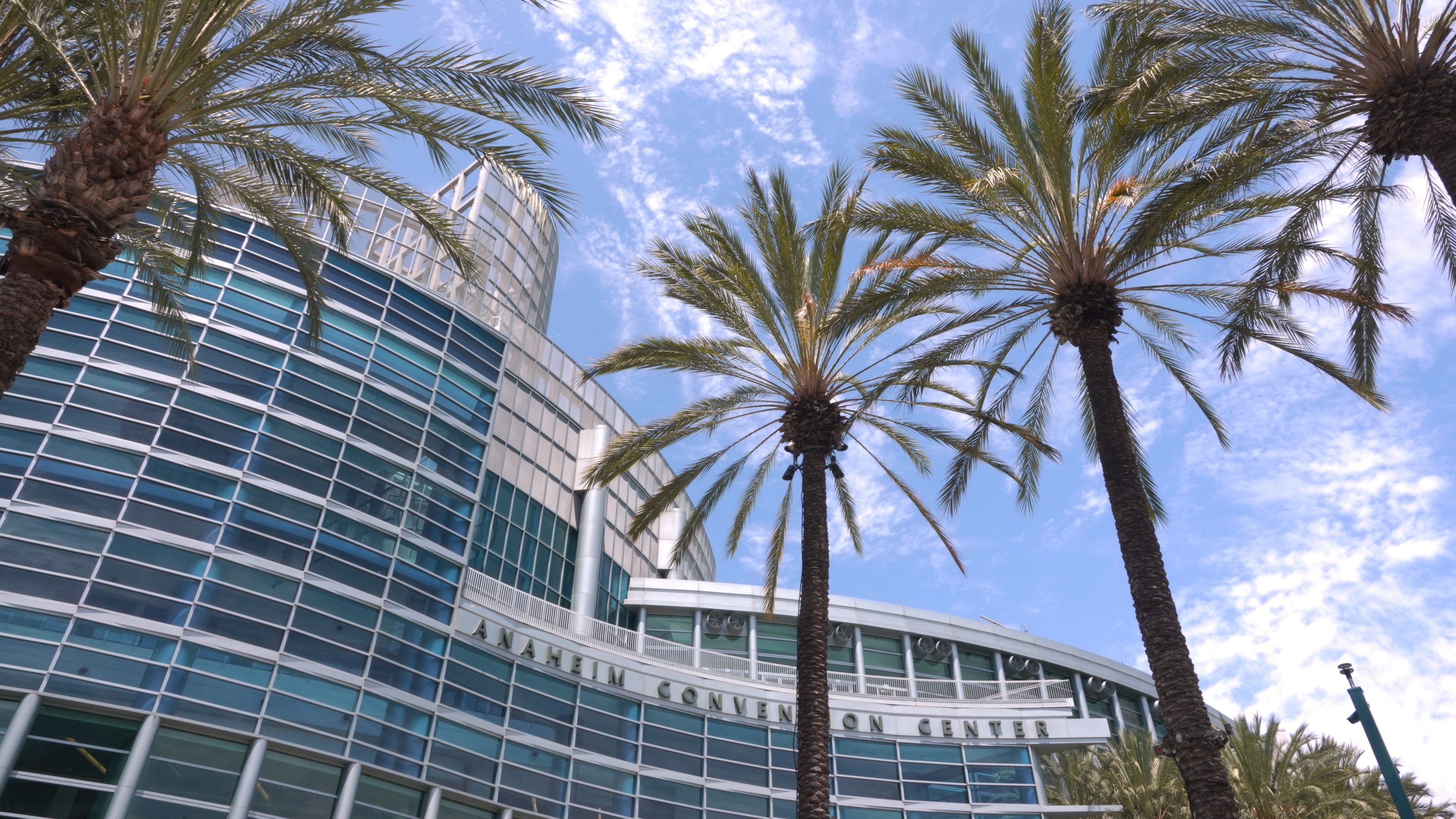 A view from below of the Anaheim Convention Center, framed by palm trees and a blue sky.